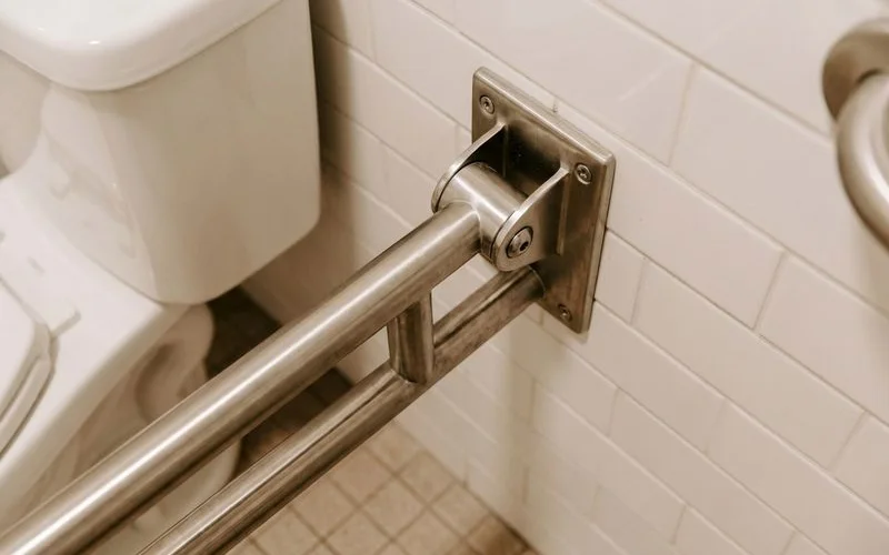 Professional chrome grab bar installed next to toilet in well-lit bathroom with non-slip tile flooring